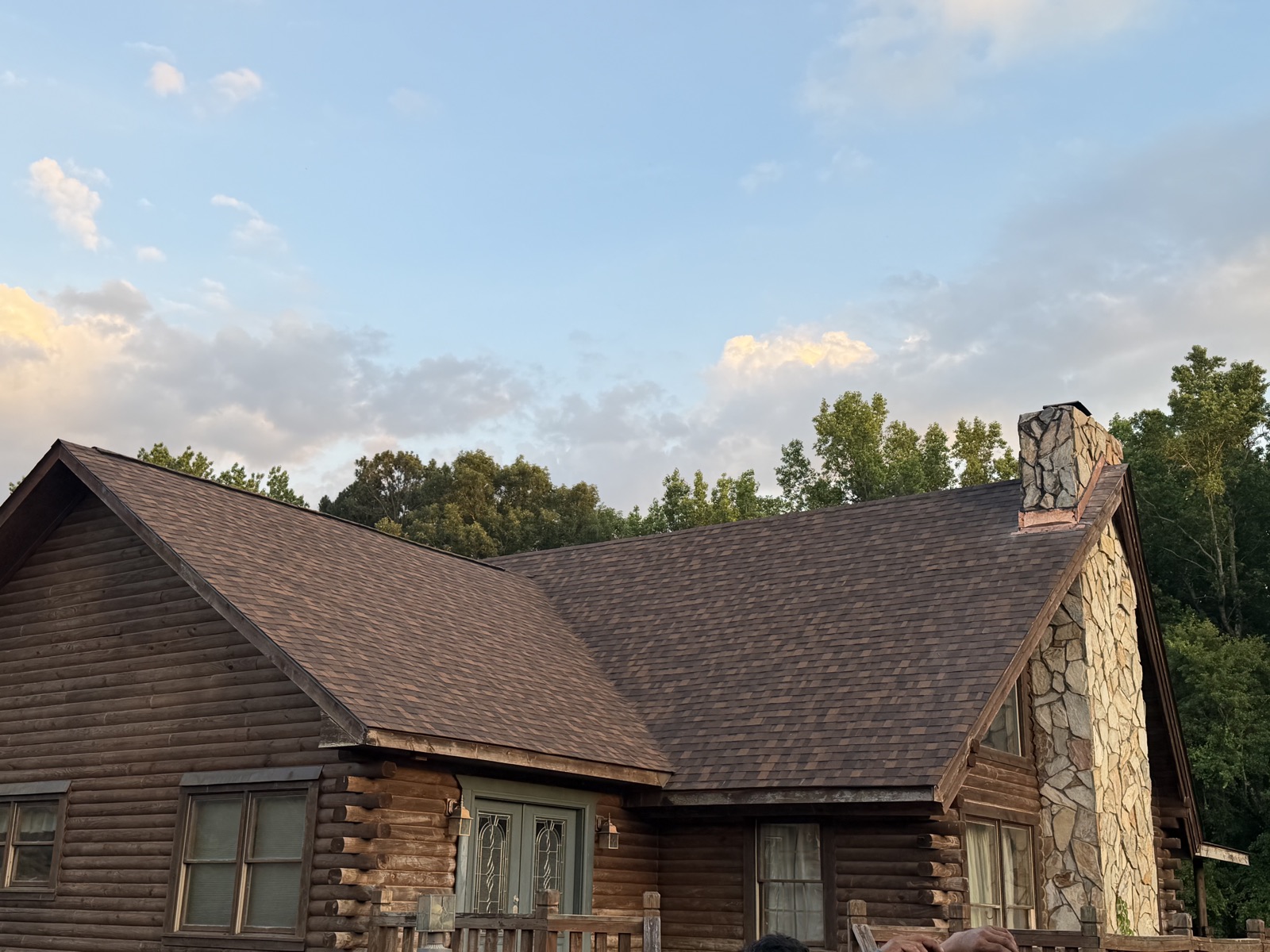 The same log cabin with its finished brown architectural shingle roof at sunset