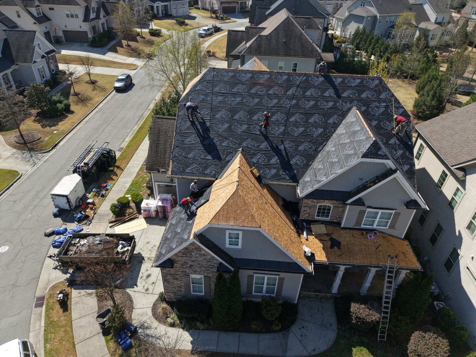 Serranos crew installing underlayment on a large roof, drone view